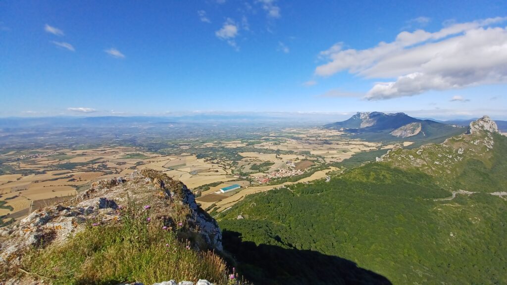 スペイン・バスク地方の山頂から見渡す360度の絶景。緑の山並みと黄金色の畑、青空が広がる雄大な風景。